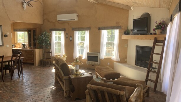 A rustic living room with a fireplace, wooden furniture, and a television on a shelf. - Country Barn House (Fountain)
