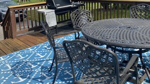 Eine Terrasse mit Grill, Gartenmöbeln und einer blau gemusterten Tischdecke.