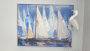 Ein Zimmer mit einem großen Gemälde von Segelbooten an der Wand, einer Holzkommode und einer weißen Lampe.