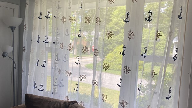 Ein Zimmer mit einem braunen Sofa, einem blauen Kissen und einem weißen Vorhang mit Anker- und Kompassmotiven.