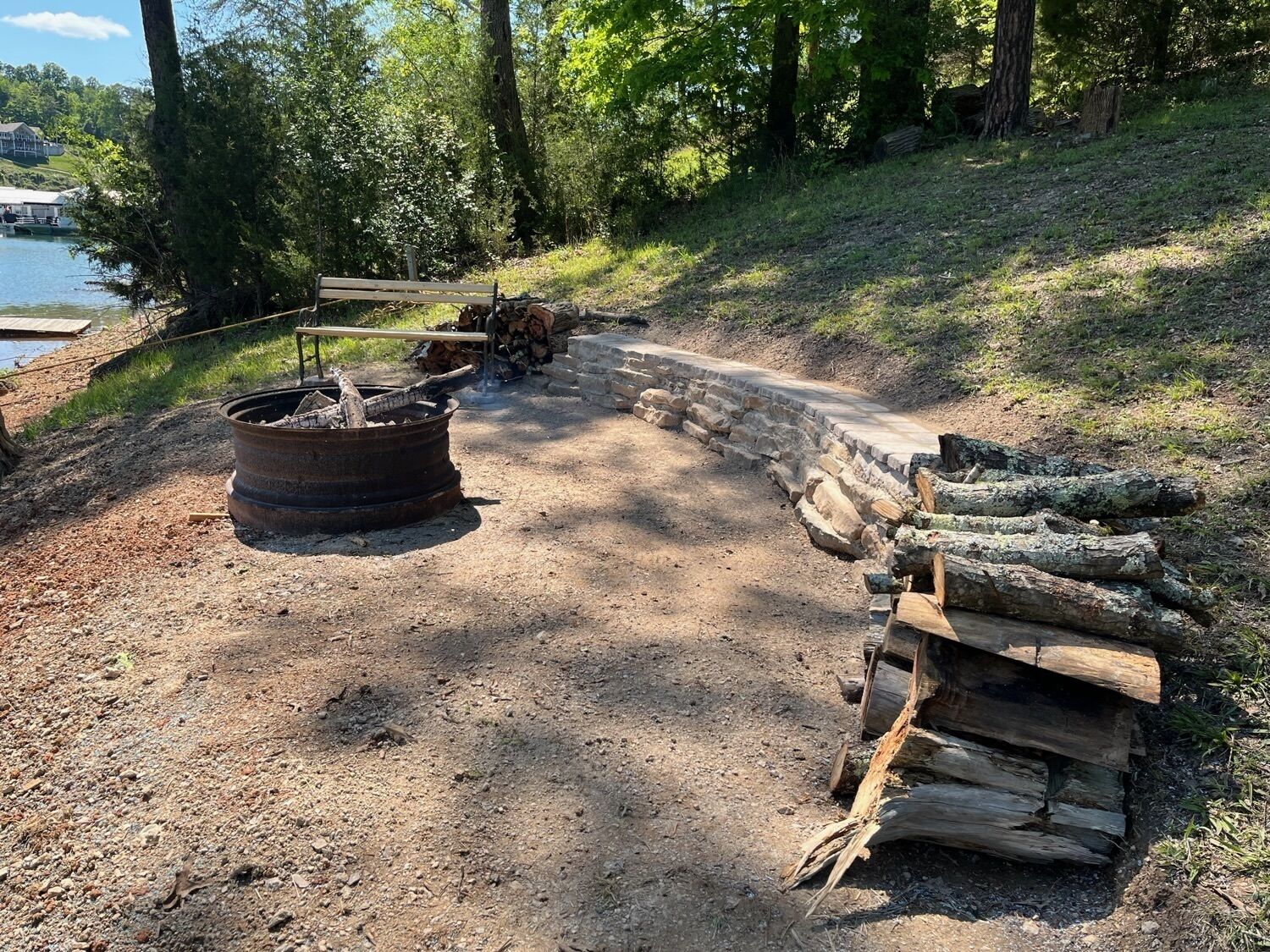 A campsite with a fire pit, a stone wall, and a wooden bench.