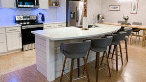 Une cuisine moderne avec des meubles blancs, des appareils en acier inoxydable et un îlot central doté de tabourets de bar.
