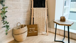 Une pièce avec un mur en briques blanches, une échelle en bois sur laquelle est posée une couverture tricotée, un panier tressé et un panneau d’accueil.