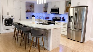 Une cuisine moderne avec des meubles blancs, un réfrigérateur en acier inoxydable, un four encastré et un îlot central doté de tabourets de bar.