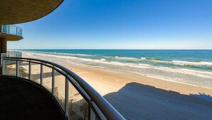 Une vue sur la plage depuis un balcon doté d’une balustrade incurvée, donnant sur l’océan et le rivage sablonneux.
