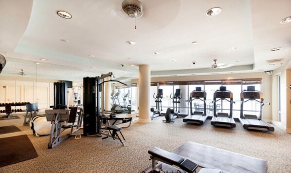 A spacious gym with various exercise equipment, large windows, and a high ceiling. - High End Lux Condo With Oceanfront Massive Balcony (Daytona Beach)