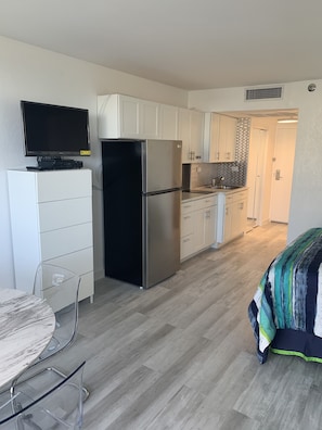 Efficient kitchen with oven and refrigerator, adjacent dining area with round table and clear glass chairs.