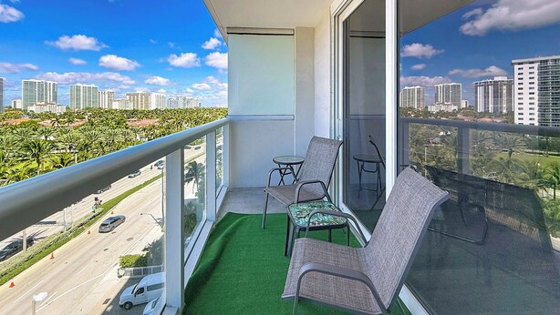 A balcony with a view of a cityscape, a small table, two chairs, and a green artificial turf. - Instaworthy-Prestigious Sunny Isles Beach. Direct beach access from building (Sunny Isles Beach)