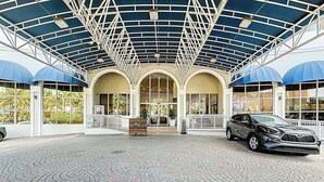 A covered entrance with a car parked in front, a tiled floor, and a building with large windows and a blue awning. - Instaworthy-Prestigious Sunny Isles Beach. Direct beach access from building (Sunny Isles Beach)