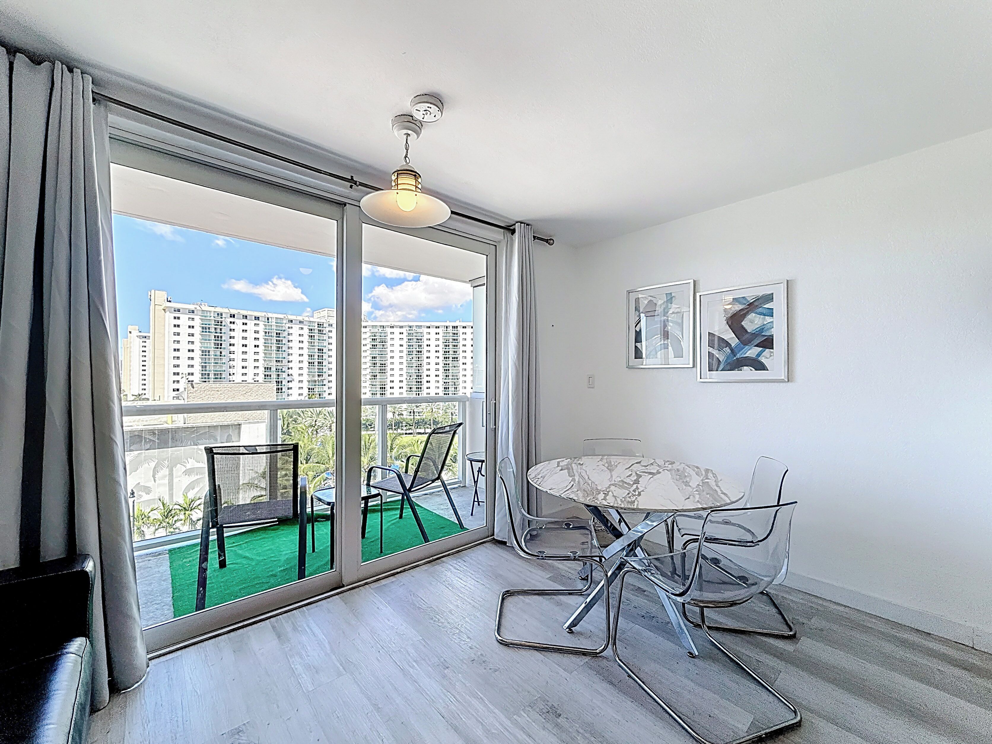 Een balkon met een tafel, stoelen, een plafondlamp en twee ingelijste foto's aan de muur.