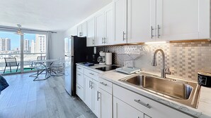A modern kitchen with white cabinets, a stainless steel sink, and a city view through large windows. - Instaworthy-Prestigious Sunny Isles Beach. Direct beach access from building (Sunny Isles Beach)