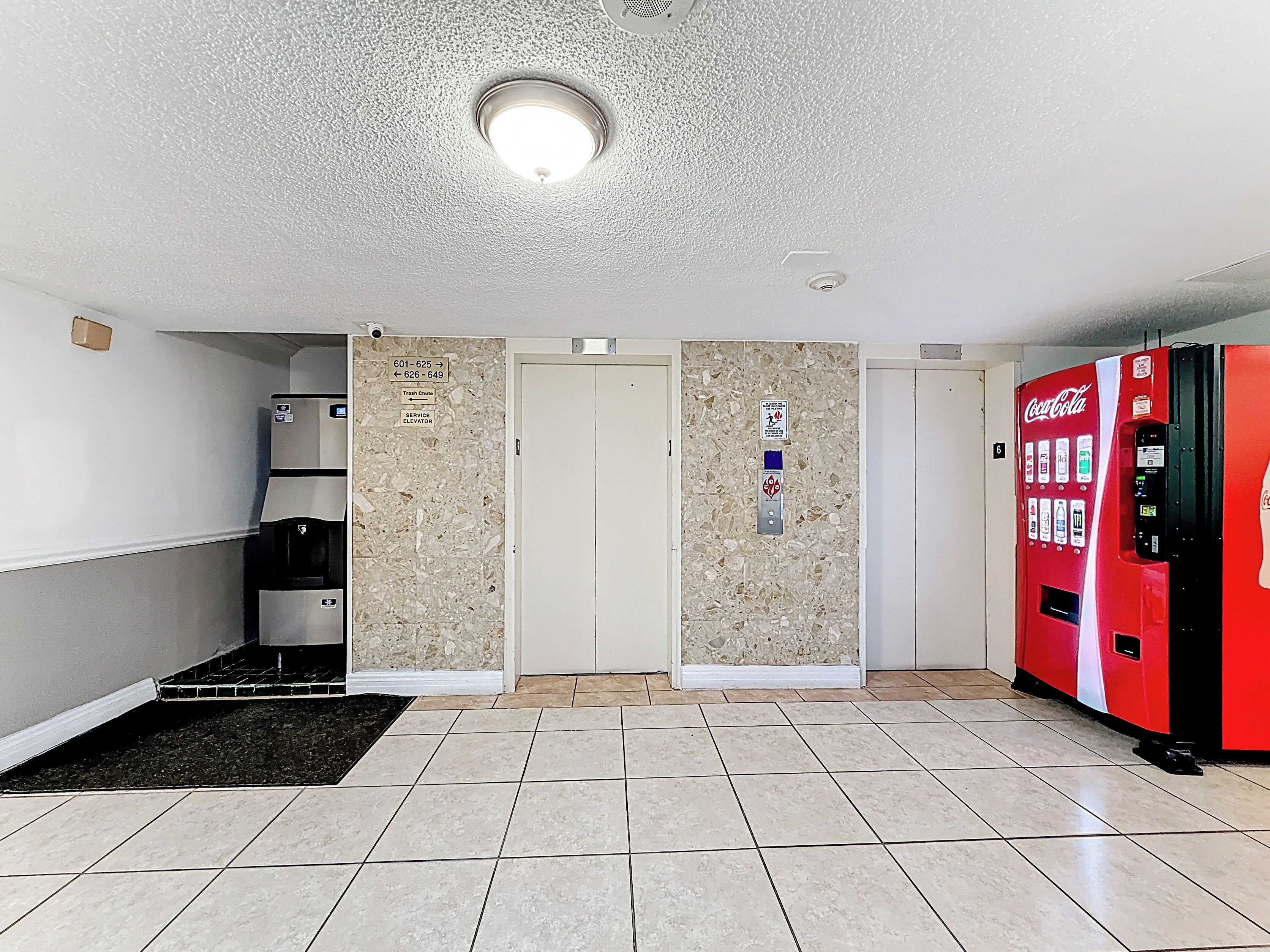 A hallway with a vending machine, a trash chute sign, and a service elevator sign.