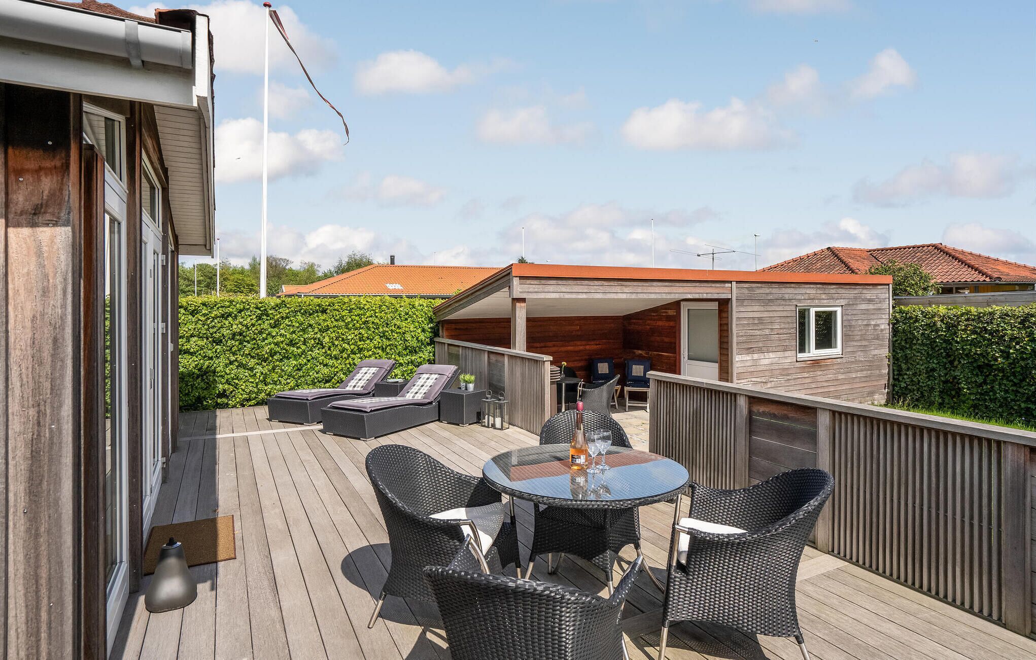 A wooden deck with outdoor furniture, a table, and a covered area with seating.