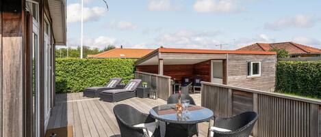 A wooden deck with outdoor furniture, a table, and a covered area with seating.