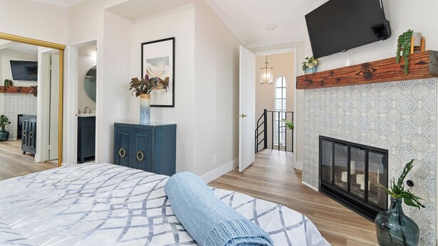 A modern bedroom with a large bed, a TV mounted on the wall, a fireplace, and a staircase leading to an upper level. - New! Refreshing Beach Getaway- Heart of San Diego! (San Diego)