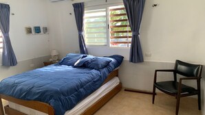 A bedroom with a bed, a chair, a window with curtains, an air conditioner, and a wall socket. - Beautiful beach house! (san crisanto)