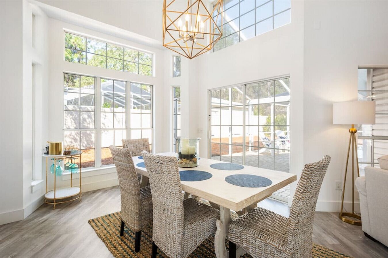 A bright dining area with a white table, wicker chairs, and a geometric pendant light.