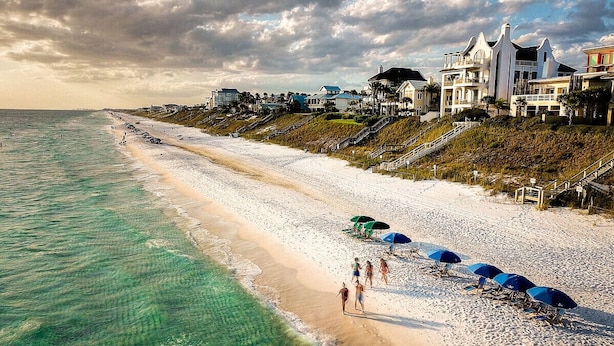 Een strand met helder turquoise water, een zandstrand en verschillende strandparasols.