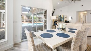 Een ruime eethoek met een grote tafel, rieten stoelen en uitzicht op een zwembad.