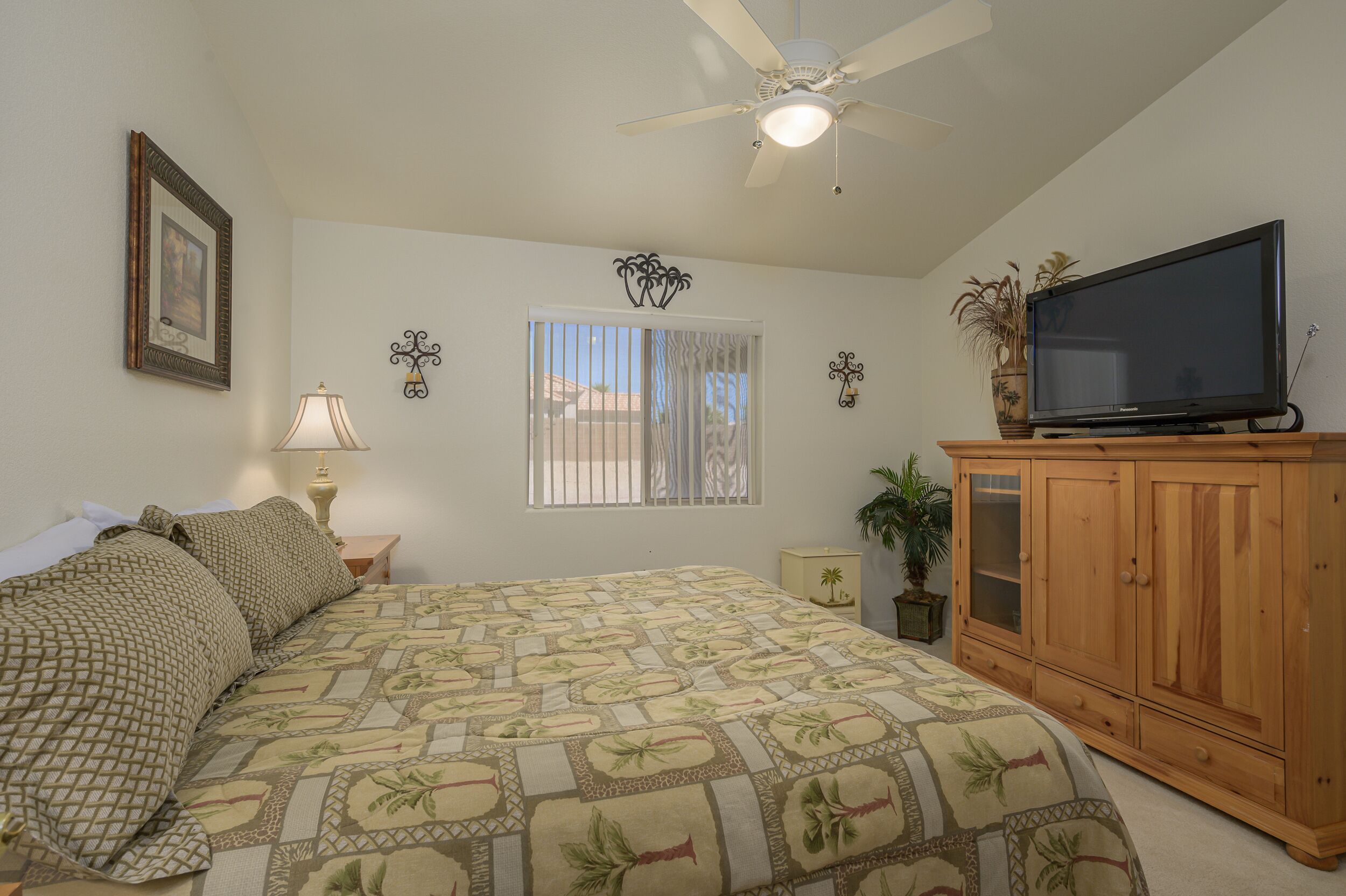 A bedroom with a bed, a ceiling fan, a television on a wooden cabinet, and a window with curtains.