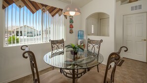 A dining area with a glass table, four chairs, a hanging light fixture, and a water dispenser. - Mohave desert retreat  (Fort Mohave)