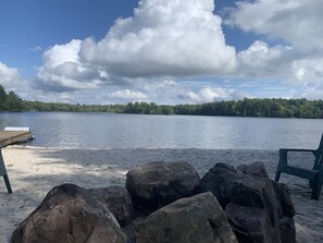 Enjoy serene lake views from a comfortable chair on the sandy beach, with a wooden dock stretching into the water.