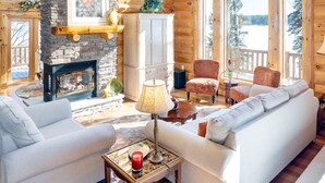 L’intérieur d’une cabane en rondins, avec une cheminée en pierre, des meubles en bois et de grandes fenêtres donnant sur le paysage extérieur.