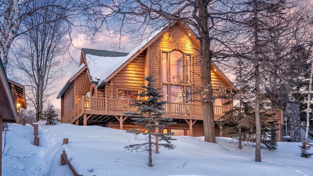 Une cabane en rondins avec une terrasse en bois et un paysage enneigé.