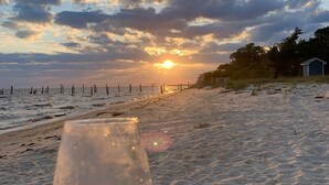 Escena de playa con un atardecer, una bebida en un vaso y una valla al fondo.