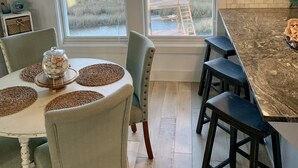 Un comedor con una mesa preparada para cuatro personas, rodeado de taburetes de bar y grandes ventanales que ofrecen vistas al exterior.