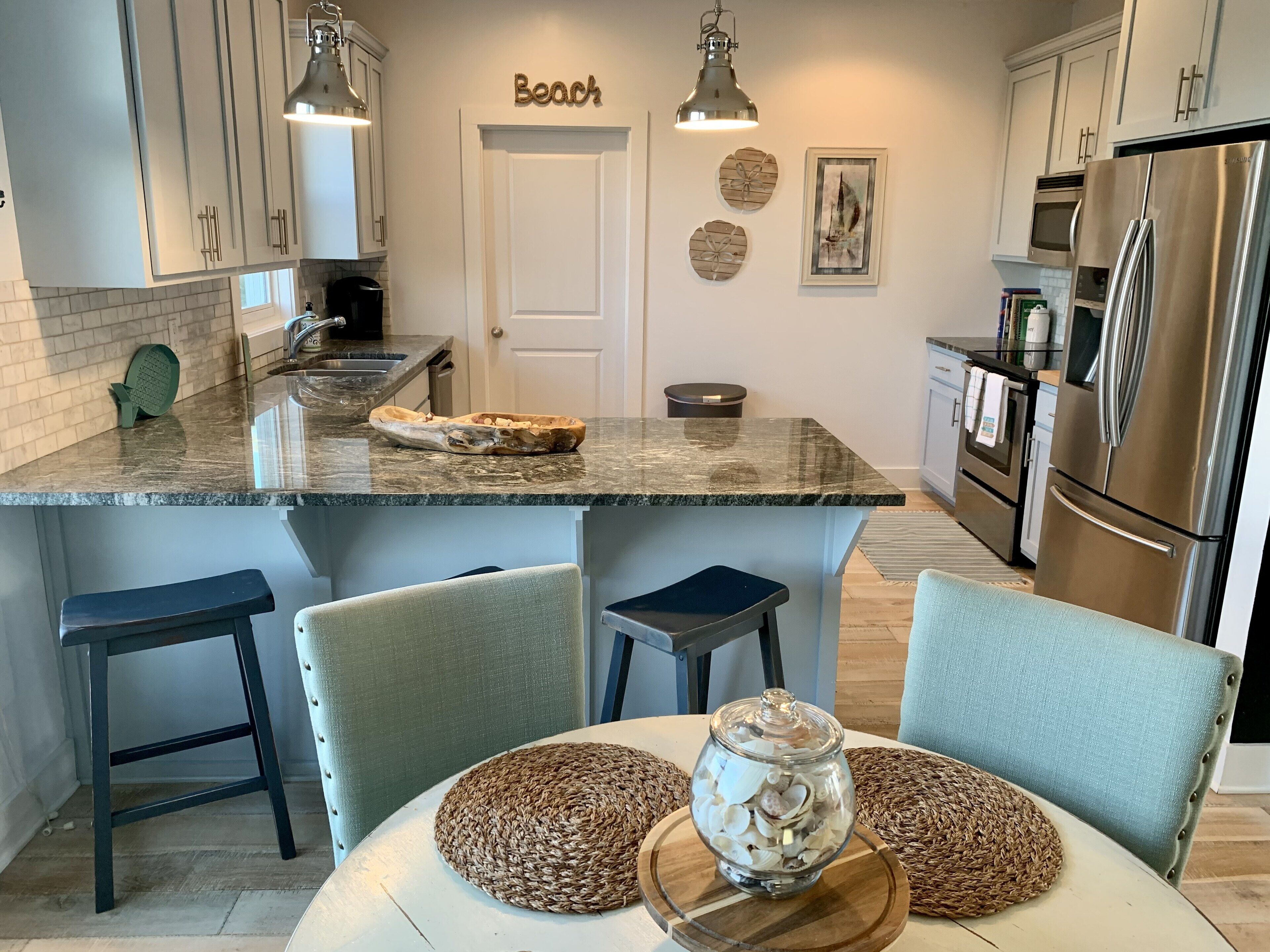 A modern kitchen with a marble countertop, stainless steel appliances, and a seating area with woven placemats.