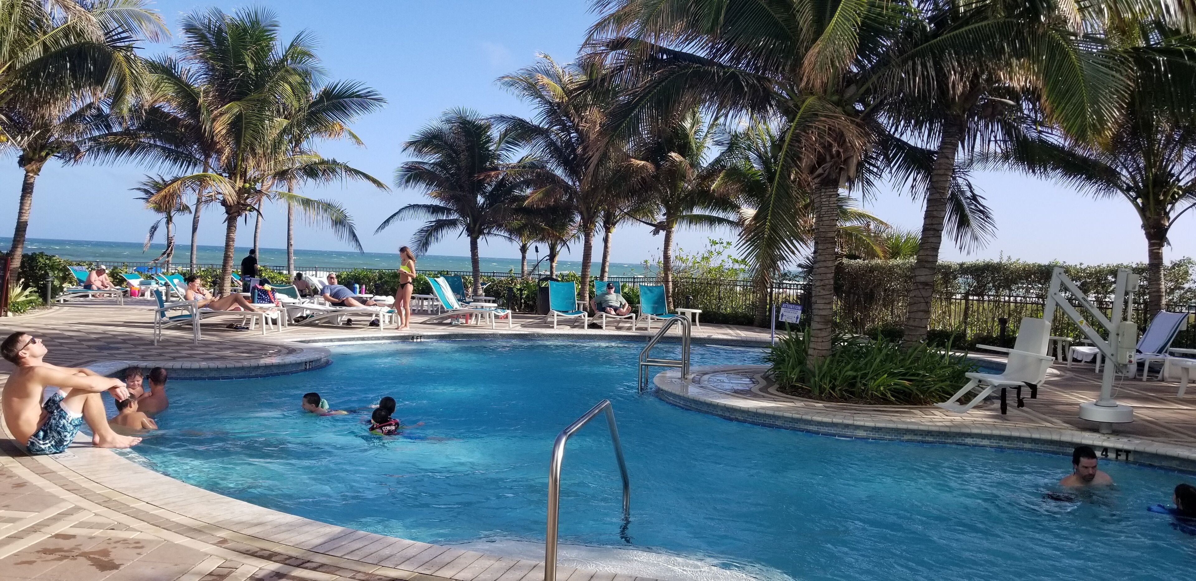 A pool area with lounge chairs and palm trees.
