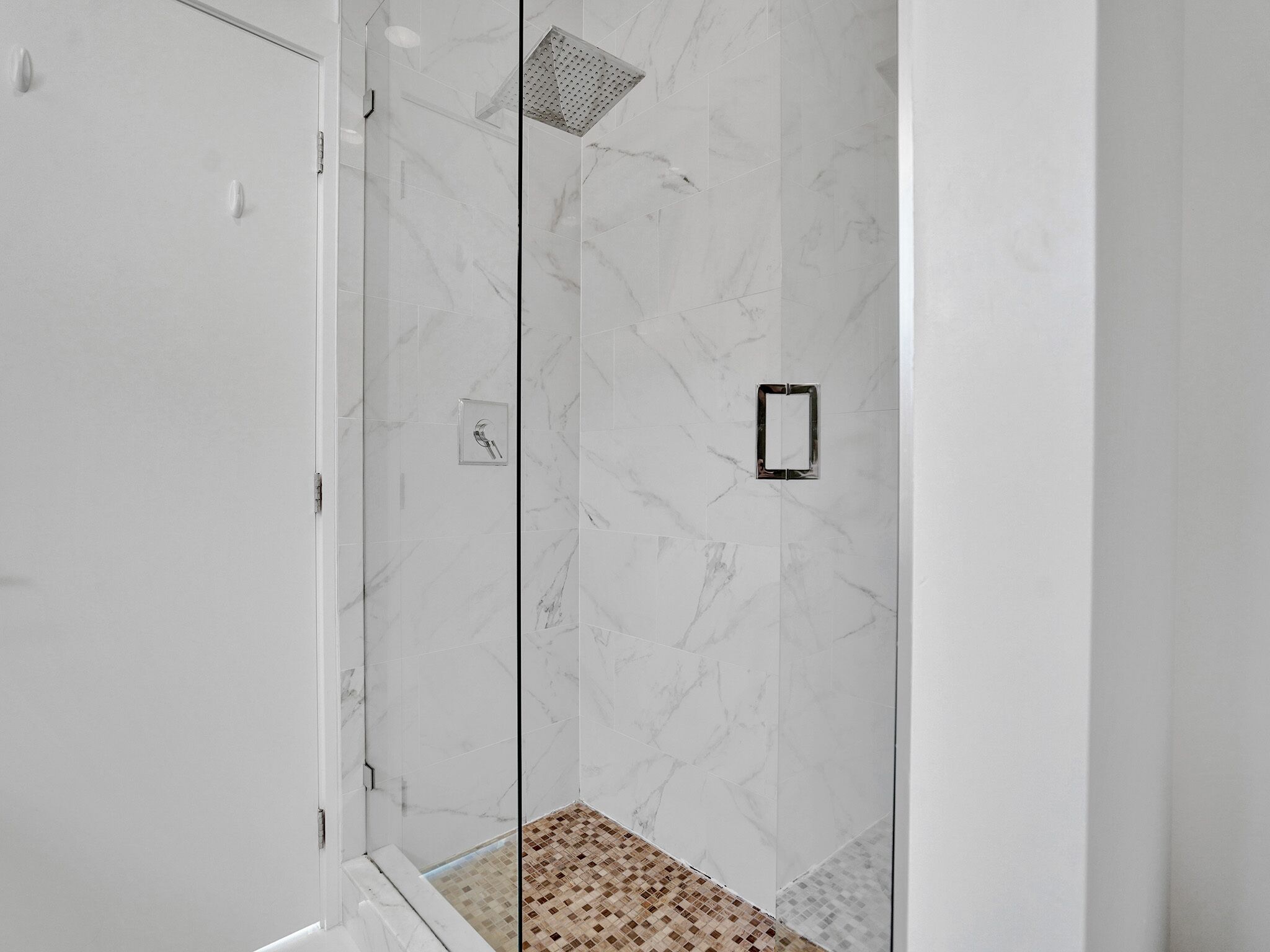 A modern shower with a glass door, a showerhead, and a tiled floor.