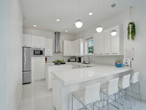 A modern kitchen with white cabinetry, stainless steel appliances, a central island with bar stools, and pendant lighting.