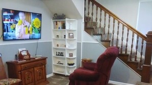 A living room with a TV, a red armchair, a wooden cabinet, and a bookshelf. - Convenient Family-Friendly Home -10 Min to Tulsa!" (Tulsa)