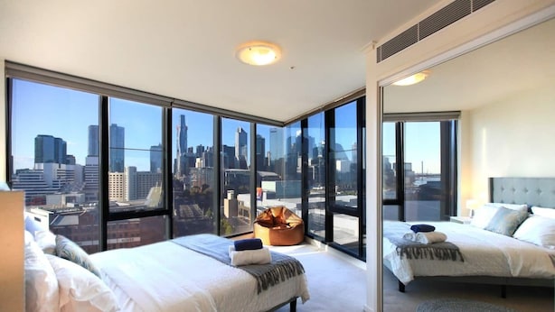 Een moderne hotelkamer met twee bedden, grote ramen met uitzicht over de stad en een gezellige zithoek.