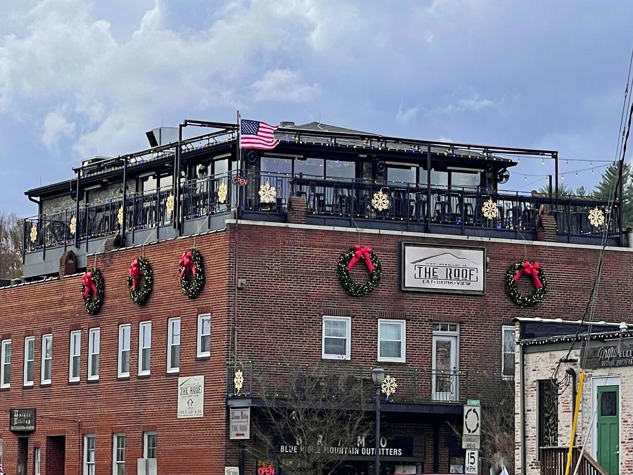A brick building with a flat roof, adorned with Christmas wreaths and lights, and a sign for 'The Roof' restaurant.