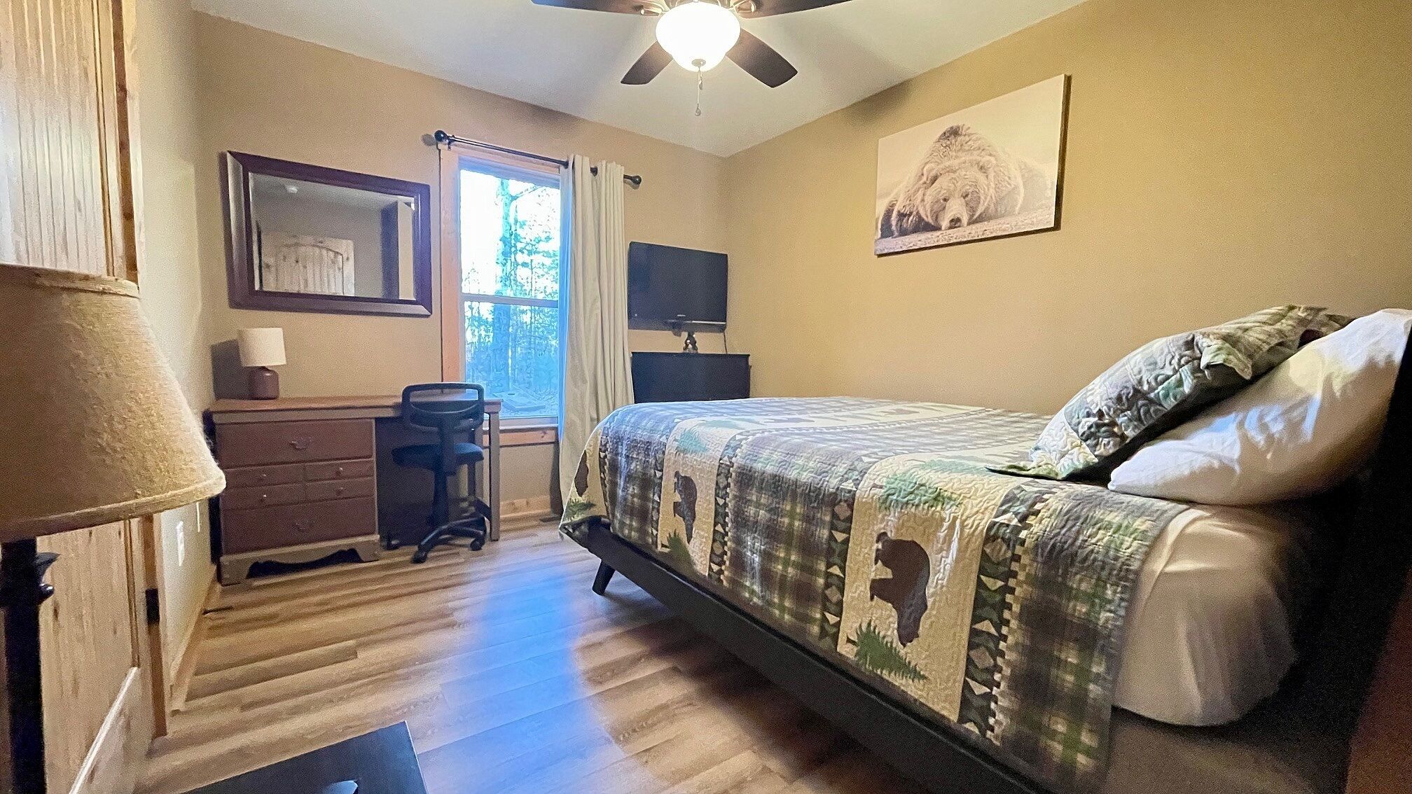 A bedroom with a bed, desk, chair, and a ceiling fan.