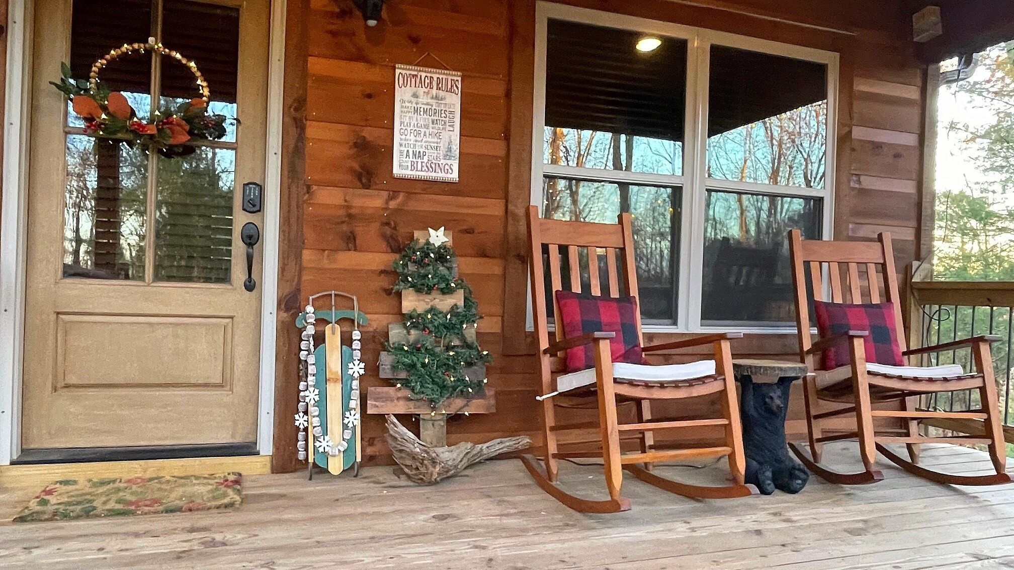 A wooden cabin with a porch, a Christmas tree, rocking chairs, and a sign listing cottage rules.
