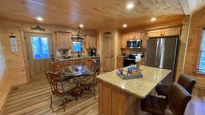 A wooden cabin kitchen with a round dining table, chairs, granite countertops, a refrigerator, and a microwave.