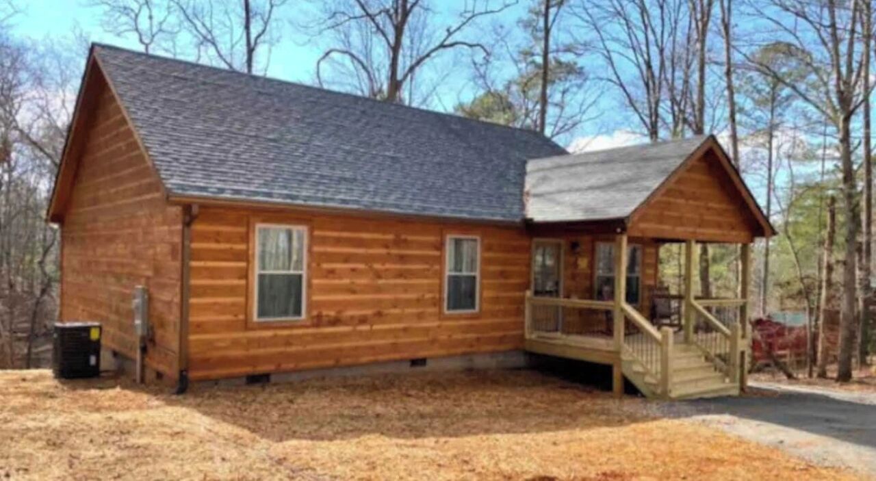 A wooden cabin with a porch and a small deck, surrounded by trees.