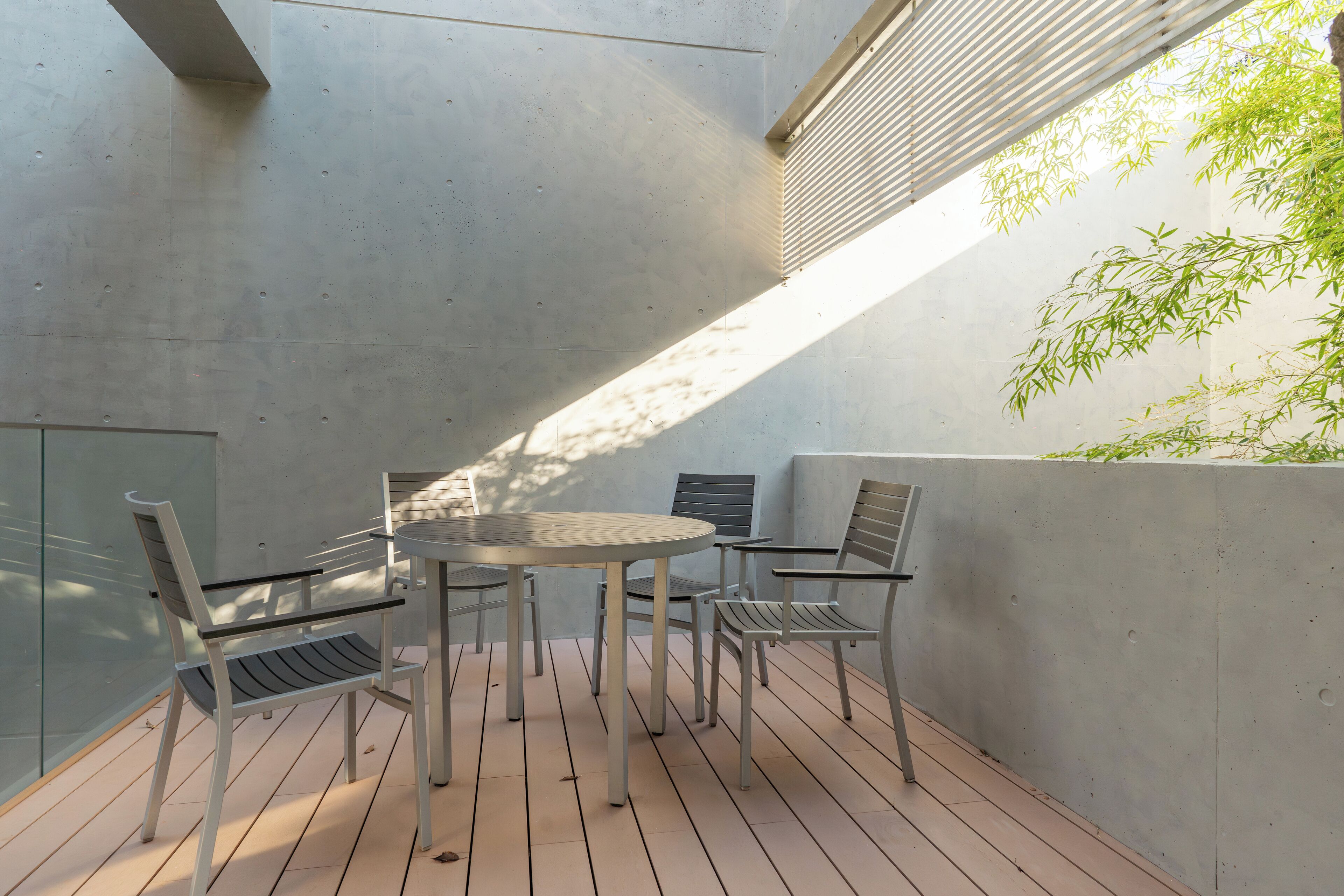 An outdoor patio with a round table and four chairs, surrounded by a concrete wall and a bamboo plant.