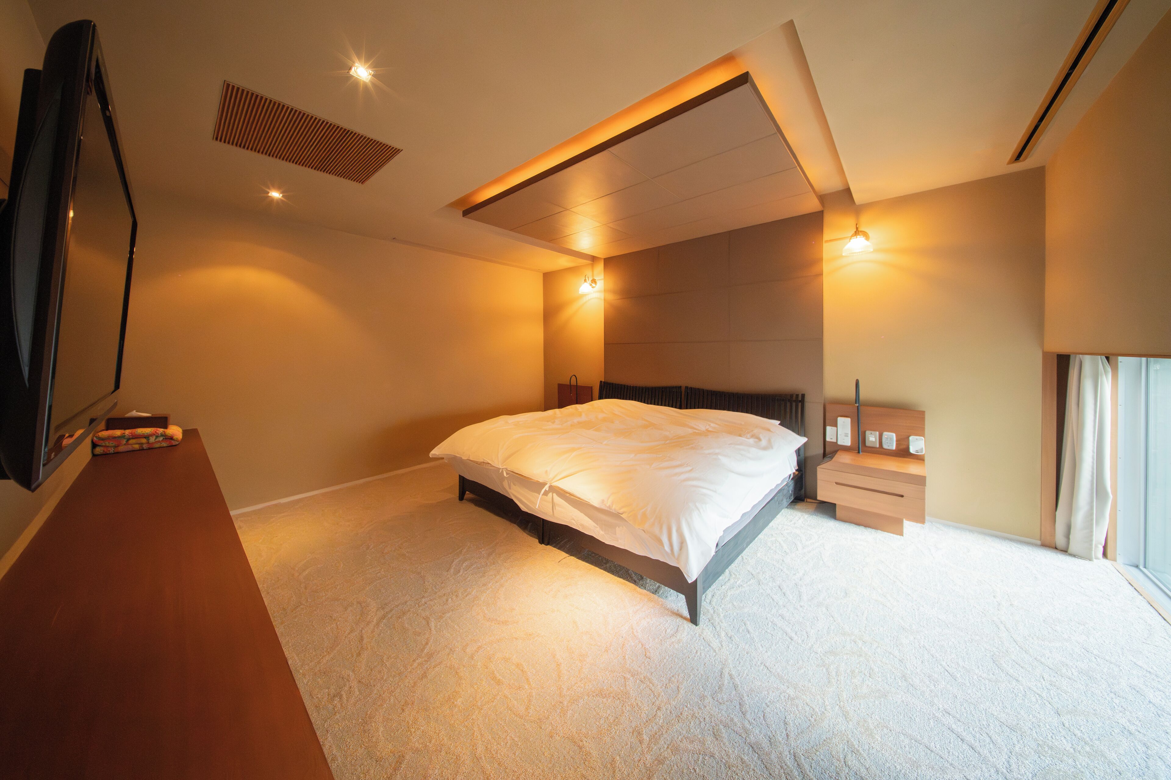 A bedroom with a bed, bedside tables, a TV, and a window.