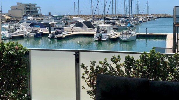 A marina with multiple boats docked, a building in the background, and a clear sky. - Mariners Cove Mindarie ~ Luxe Marina Waterfront (Mindarie)