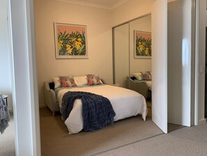 A bedroom with a bed, pillows, a blanket, a nightstand, a mirror, and two framed floral paintings on the wall. - Mariners Cove Mindarie ~ Luxe Marina Waterfront (Mindarie)