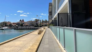 A waterfront promenade with a clear sky, a marina with boats, and buildings with balconies overlooking the water. - Mariners Cove Mindarie ~ Luxe Marina Waterfront (Mindarie)