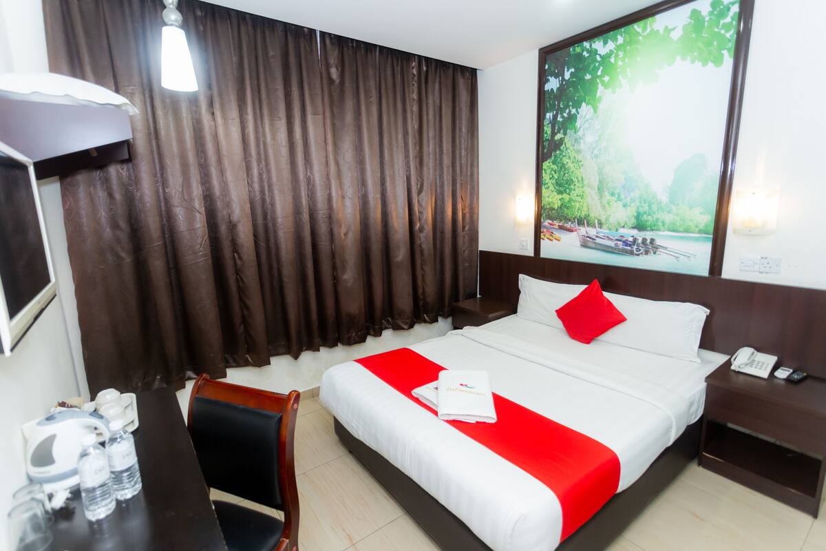 A hotel room with a large bed, a desk with a chair, a nightstand, a telephone, and a painting of a landscape.