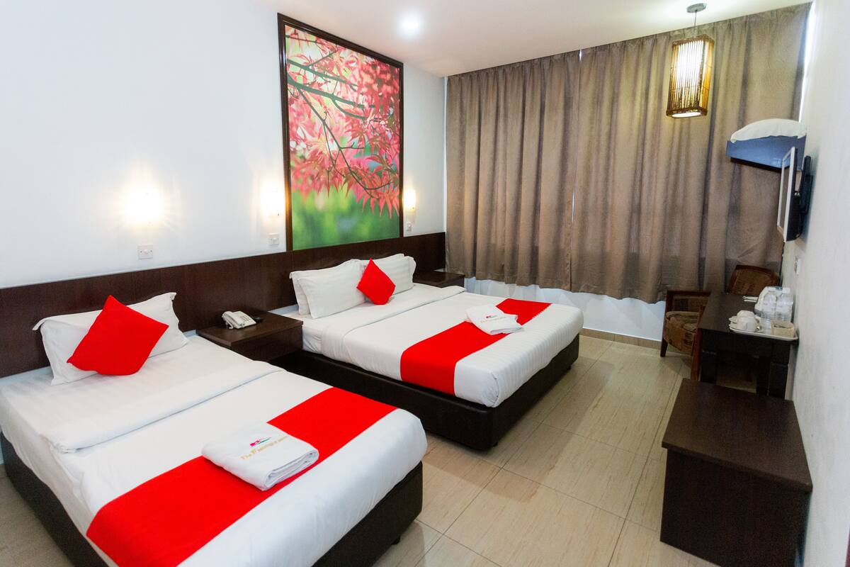 A hotel room with two beds, each with white bedding and red accents, a painting on the wall, a desk with a chair, and a television.