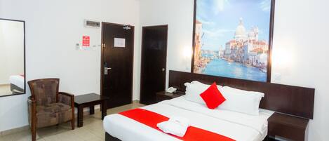A hotel room with a bed, a chair, a desk, and a large window with a cityscape view.