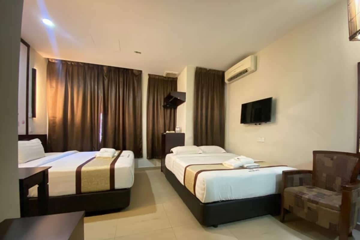 A hotel room with two beds, a desk, a chair, a flat-screen TV, and an air conditioning unit.